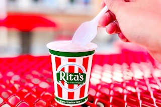 A hand holding a spoon scooping Italian ice from a Rita's cup. 