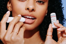woman applying and holding Aquaphor lip balm
