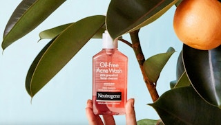 a hand holding a pink bottle of face wash 