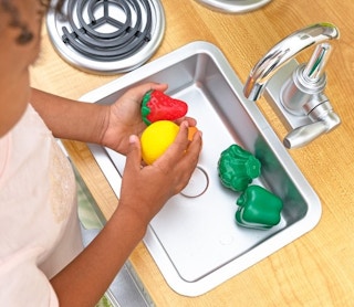 A girl playing with play food in a KidKraft toy kitchen.