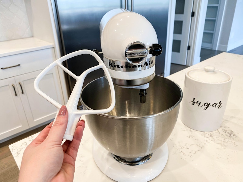 A Kitchenaid mixer on a counter with a hand holding an attachment piece.