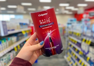 A hand holding a Colgate Optic White whitening pen.