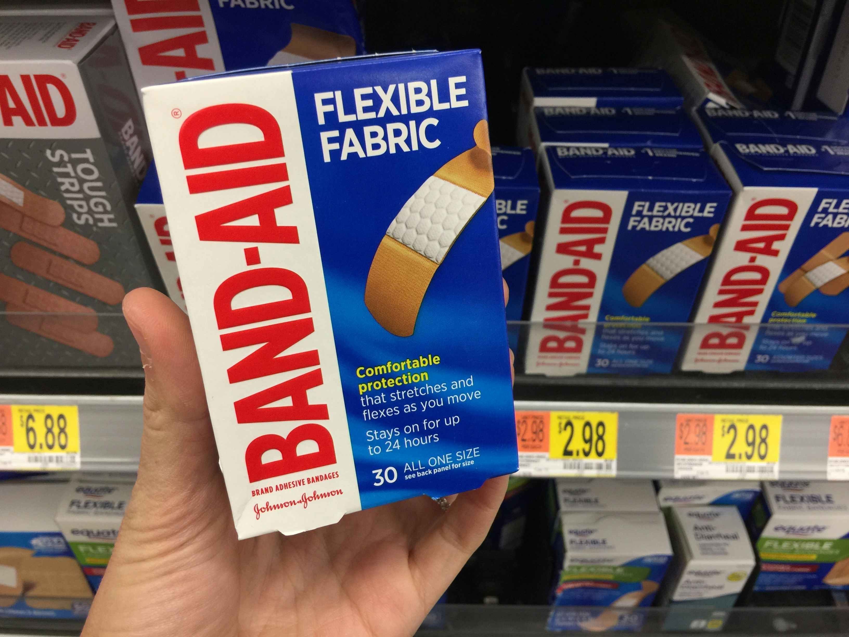 A person's hand holding up a box of band aid bandages in store. 