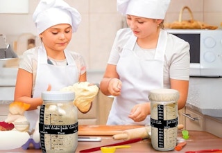 two teenagers wearing chef hats and aprons in kitchen making sourdough bread