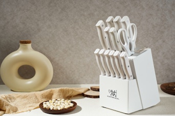 A white knife set in a white block with a built-in sharpener sits on the right side of a counter. On the left is a round bottle with a hole.