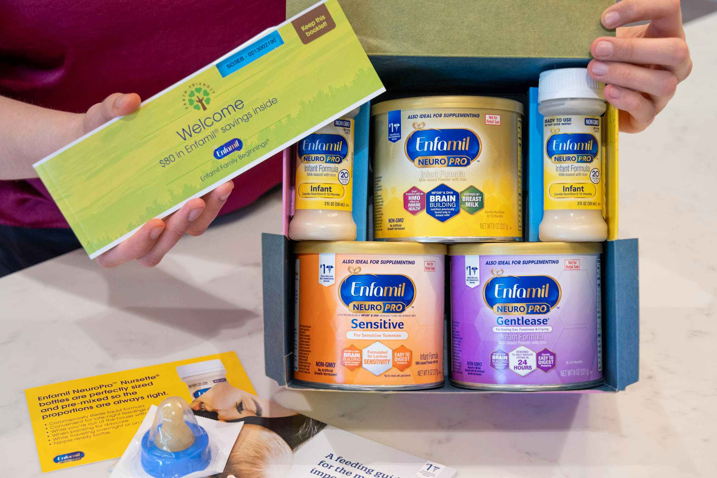 A woman holding up an Enfamil formula baby sample freebie box, showing the contents inside.