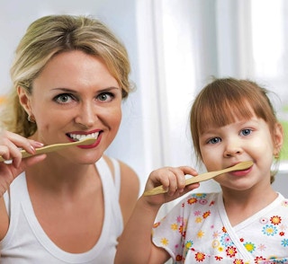 a mom and daughter using bamboo toothbrushes