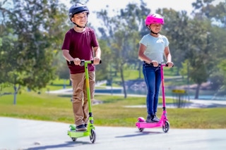 Two kids' riding Razor electric scooters in green and pink outdoors (lifestyle image)