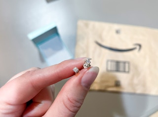 fingers pinching a pair of earrings in front of a jewelry box and amazon packaged envelope
