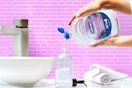 In a pink bathroom, two hands pour a Softsoap White Tea and Berry refill into a sink dispenser.