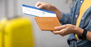 person holding plane ticket and passport cover