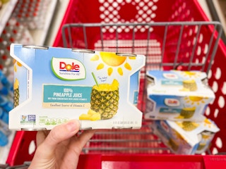 hand holding pack of Dole pineapple juice in front of shopping cart