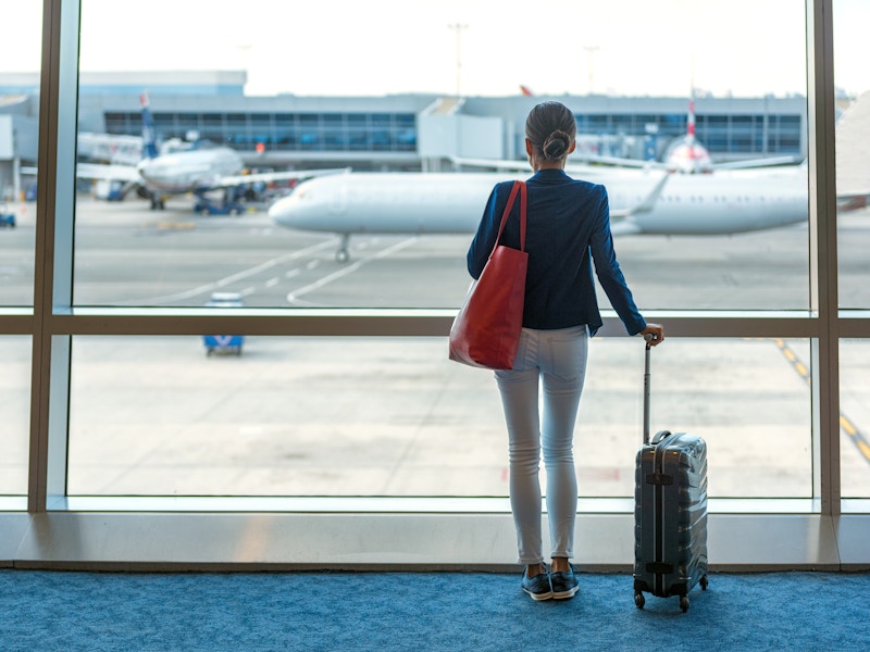 person with luggage looking out airport window at planes