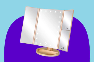 A tri-fold vanity mirror with gold stand and trip and LEDs surrounding middle panel. Right panel magnifies 2x and 3x.