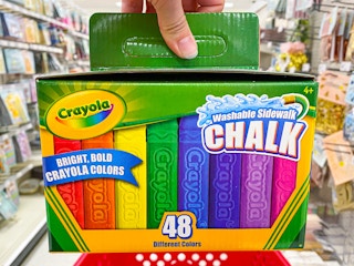 A person's hand holding a box of 48-count Crayola Sidewalk Chalk in an aisle at Target.