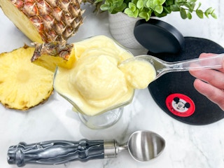 homemade dole whip in an ice cream cup on a counter next to a Mickey ears hat and a pineapple