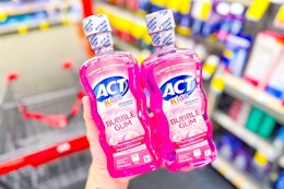 person holding 2 bottles of act mouthwash over a cvs cart