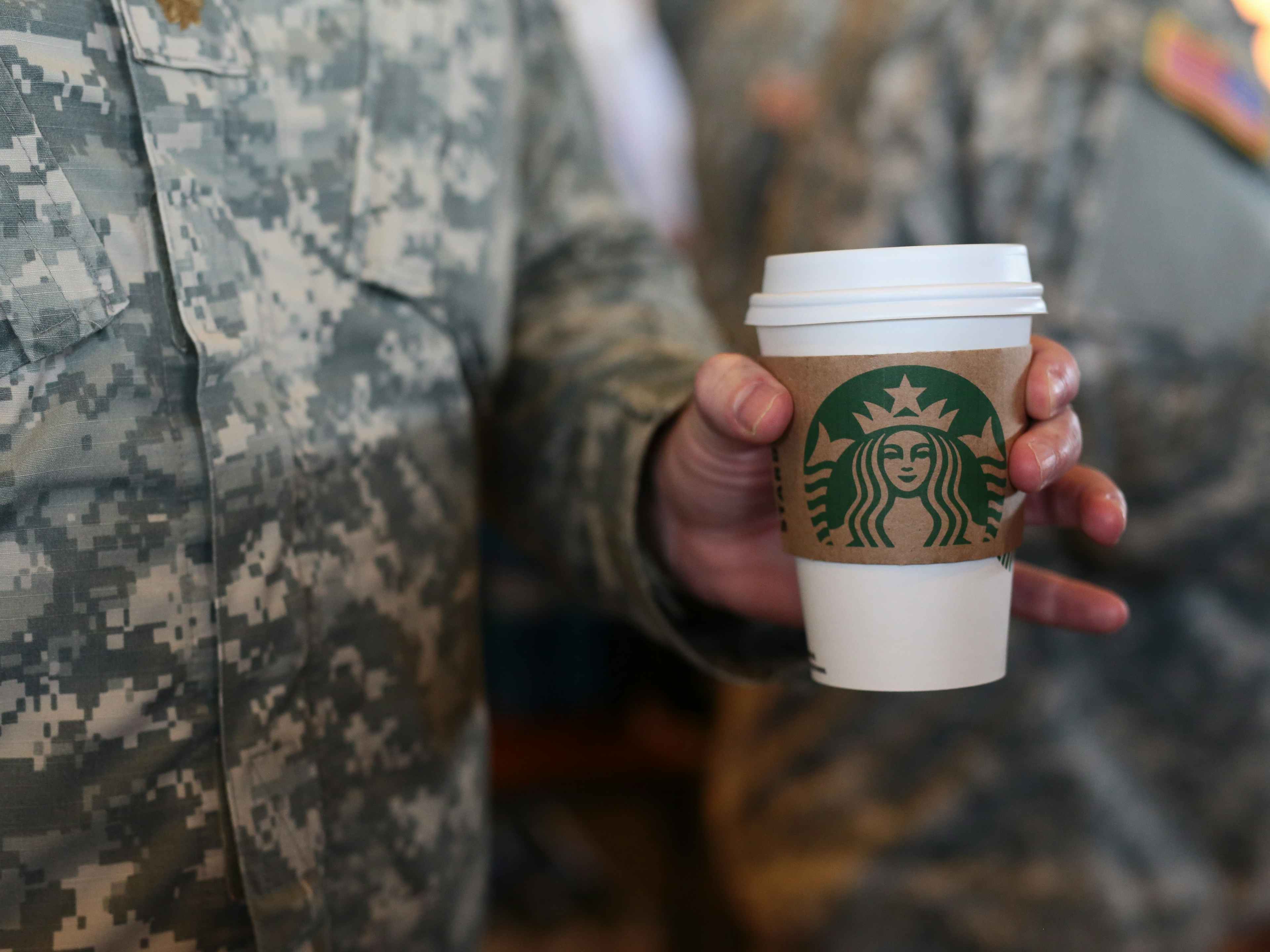 A person in military dress holding a Starbucks coffee.