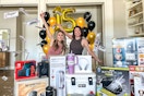 The Krazy Coupon Lady's co founders, Heather and Joanie tossing money over a pile of items they are giving away for KCL's 15th birthday