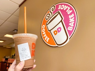 hand holding specialty iced coffee near Dunkin sign inside restaurant