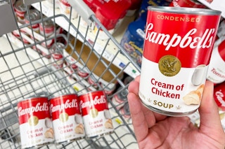 a person holding a can of soup along with other cans in cart