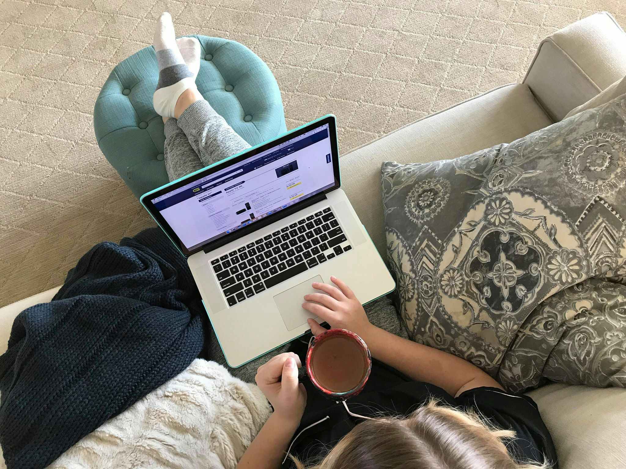 A person sitting on a couch, shopping online using a laptop.