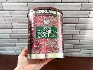 Someone holding a 3 pound can of Kirkland Columbian coffee