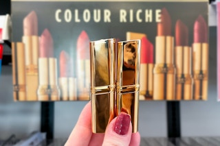 hand holding L'oreal Paris Colour Riche lipstick held in front of the store sign