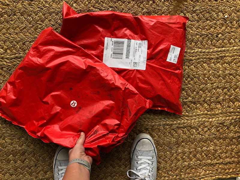 Two Lululemon packages on the floor with a hand reaching down to pick one up