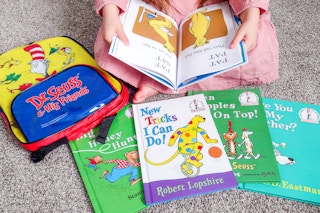 a child looking at a dr seuss book with other dr seuss books on the floor nearby
