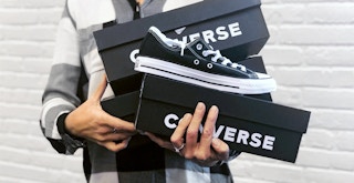 person holding several boxes of converse and black chuck taylor all-star sneakers