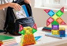 a kid packing a backpack on a table with magnetic tiles