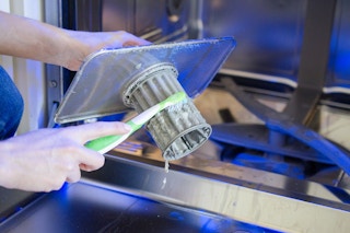 Someone scrubbing a dishwasher trap with an old toothbrush