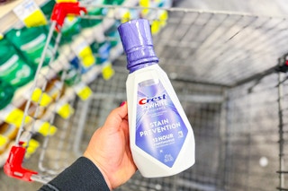 person holding a bottle of crest premium mouthwash over a cart