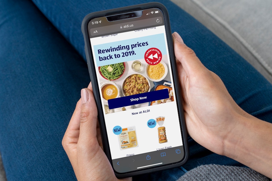 A person holding a cell phone displaying the ALDI website's graphic advertising their Thanksgiving Price Rewind offer program