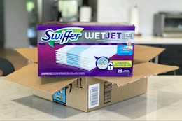 A container of Swiffer WetJet refills on top of an open Amazon box.