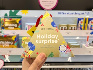 Sephora Holiday Surprise Makeup Gift Set held up by hand in front of makeup display.