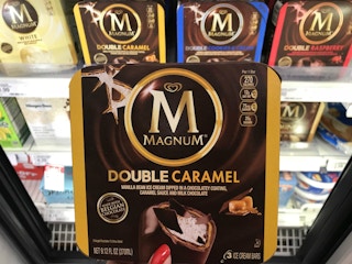 A box of Magnum ice cream bars being held in front of a shelf of more Magnum bars in the freezer section at Target