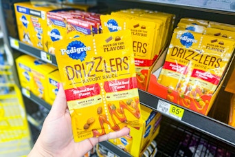 hand holding pedigree drizzlers dog food in front of dollar general shelf