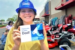 a young girl wearing a blue plastic Lowe's hat and holding up a sign that says "I love you to bits, Dad!" outside of a Lowe's store