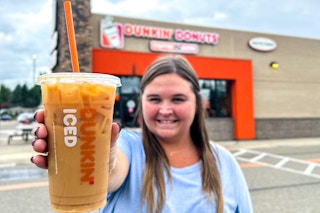 a person standing outside of dunkin with an iced coffee