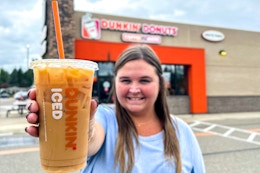 a person standing outside of dunkin with an iced coffee
