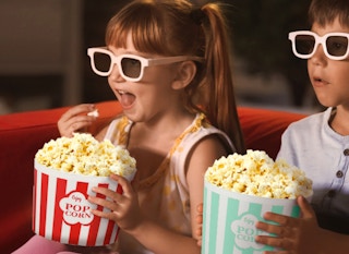 two kids eating popcorn while watching a movie