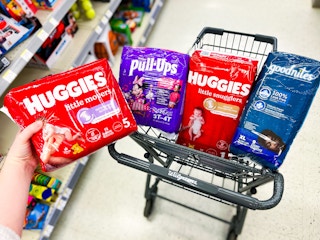 hand holding huggies diaper pack with more in a shopping cart