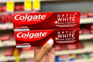 person holding two Colgate Optic White toothpastes