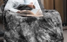a person with a gray faux fur blanket in a chair 