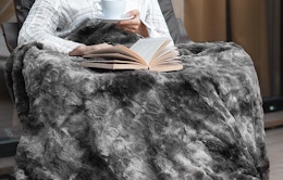 a person with a gray faux fur blanket in a chair 