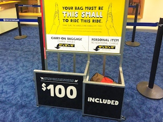 a Spirit airlines sign for baggage with a sign that says $100 if your bag doesn't fit the requirements
