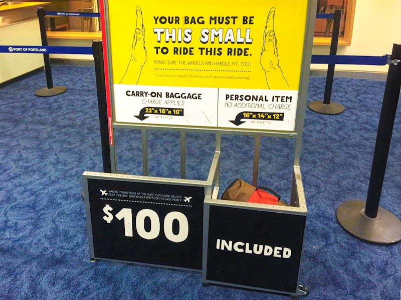 a Spirit airlines sign for baggage with a sign that says $100 if your bag doesn't fit the requirements