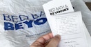 A person holding a Bed Bath & Beyond receipt with the return policy showing and a shopping bag in the background